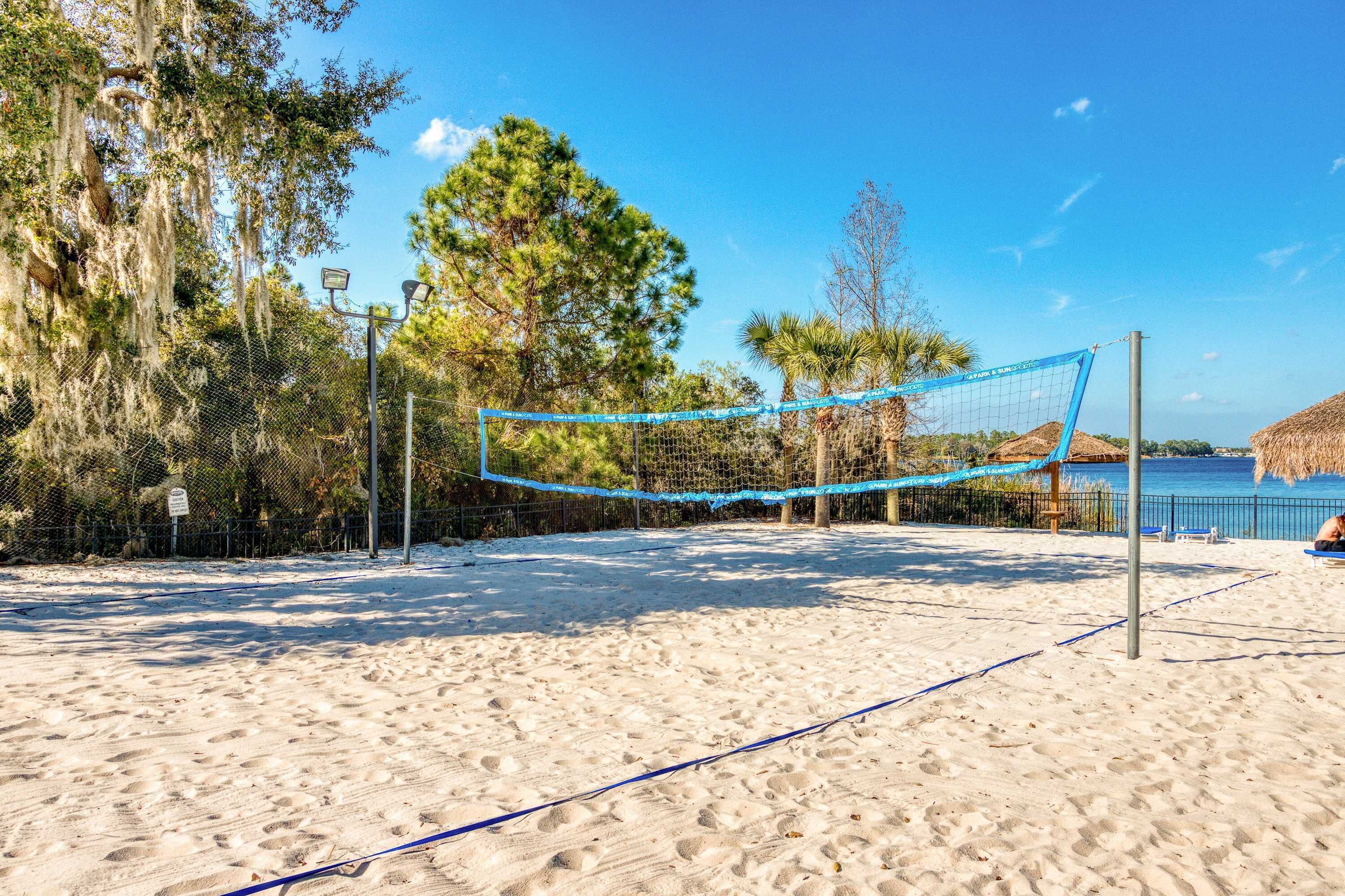 A beach volleyball court with a net, surrounded by sand and trees.