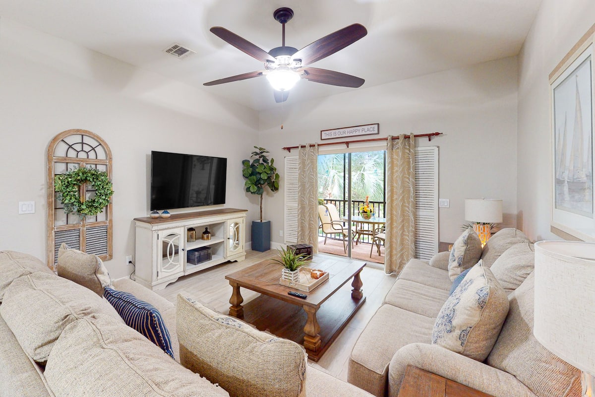 A living room with a ceiling fan, a television, a coffee table with decorative items, and a sofa.