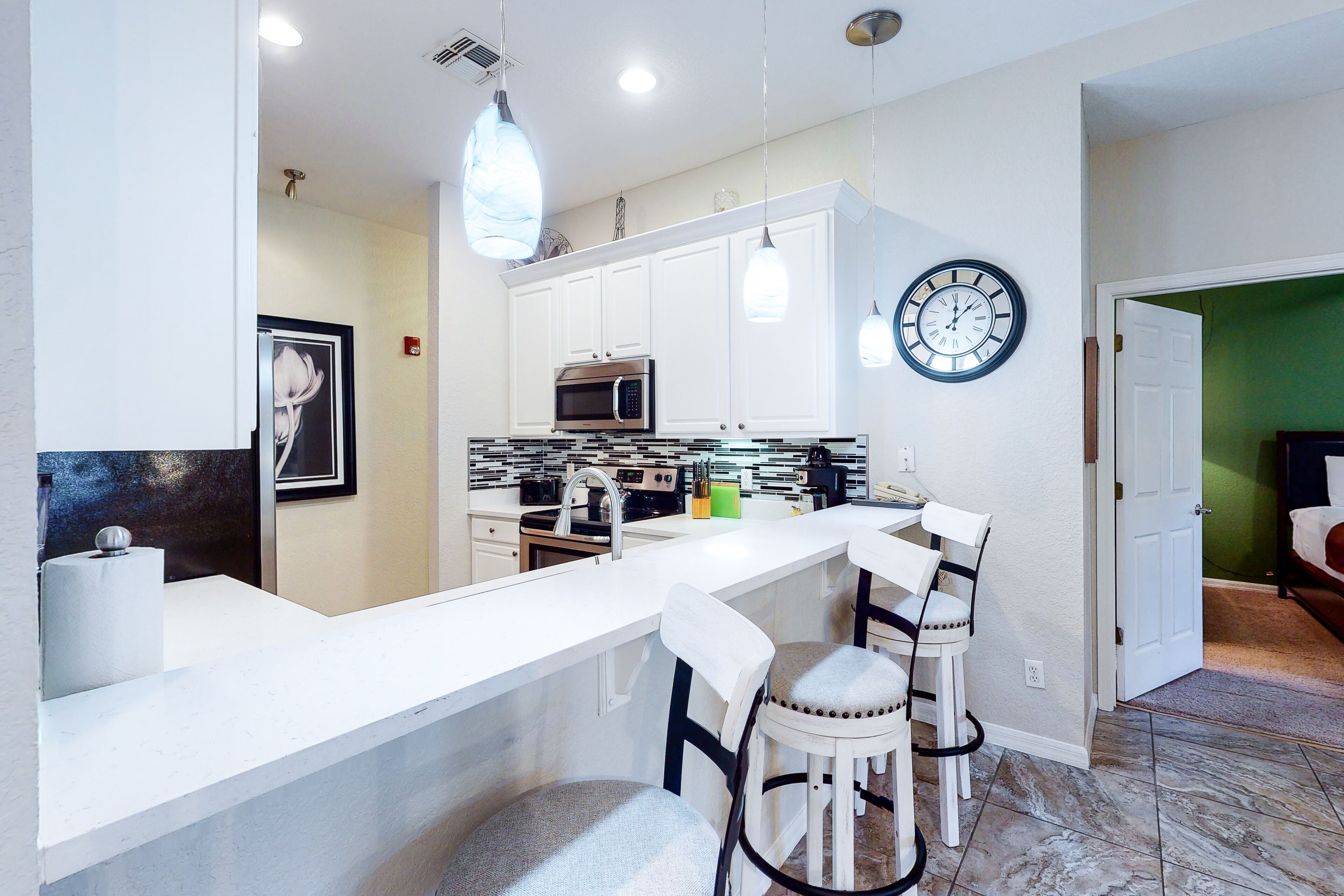 Cocina moderna con armarios blancos, un microondas de acero inoxidable, un lavabo y una barra con dos taburetes.