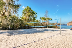 A beach volleyball court with a net, surrounded by sand and trees.