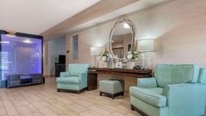A hotel lobby with teal armchairs, a wooden reception desk, a large mirror, and a blue curtain. - Best Western Plus Oceanside Palms (Oceanside)