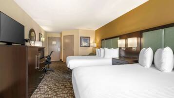 A hotel room with two beds, a desk, a television, and a patterned carpet.