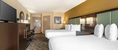 A hotel room with two beds, a desk, a television, and a patterned carpet.