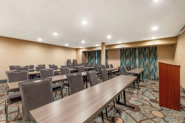 Una sala de conferencias con varias mesas y sillas, un atril y alfombra estampada.