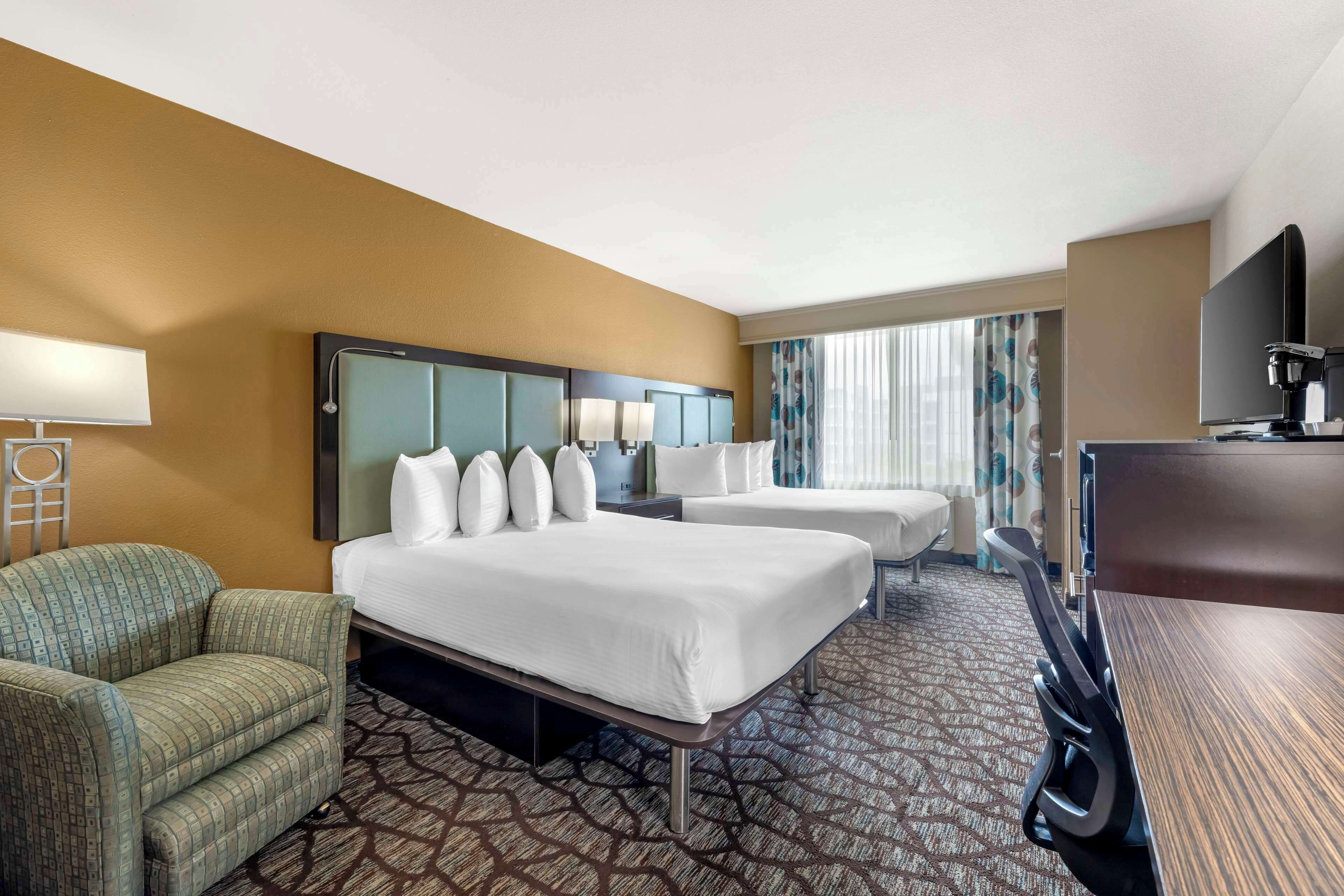 A hotel room with two beds, a desk, a chair, a TV, and a coffee machine.