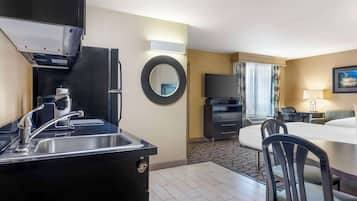 A hotel room with a kitchenette, a dining area with a table and chairs, a TV, and a bed.