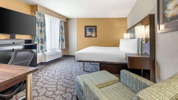 Quarto de hotel com cama, escrivaninha, cadeira, televisão e janela com cortinas.