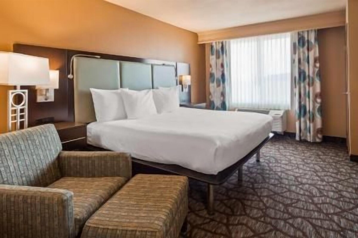 A hotel room with a large bed, a desk, a chair, a television, and a window with curtains.