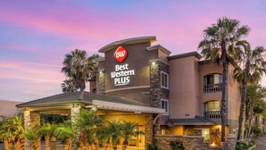 A Best Western Plus hotel with a stone facade, palm trees, and a well-lit entrance. - Best Western Plus Oceanside Palms (Oceanside)