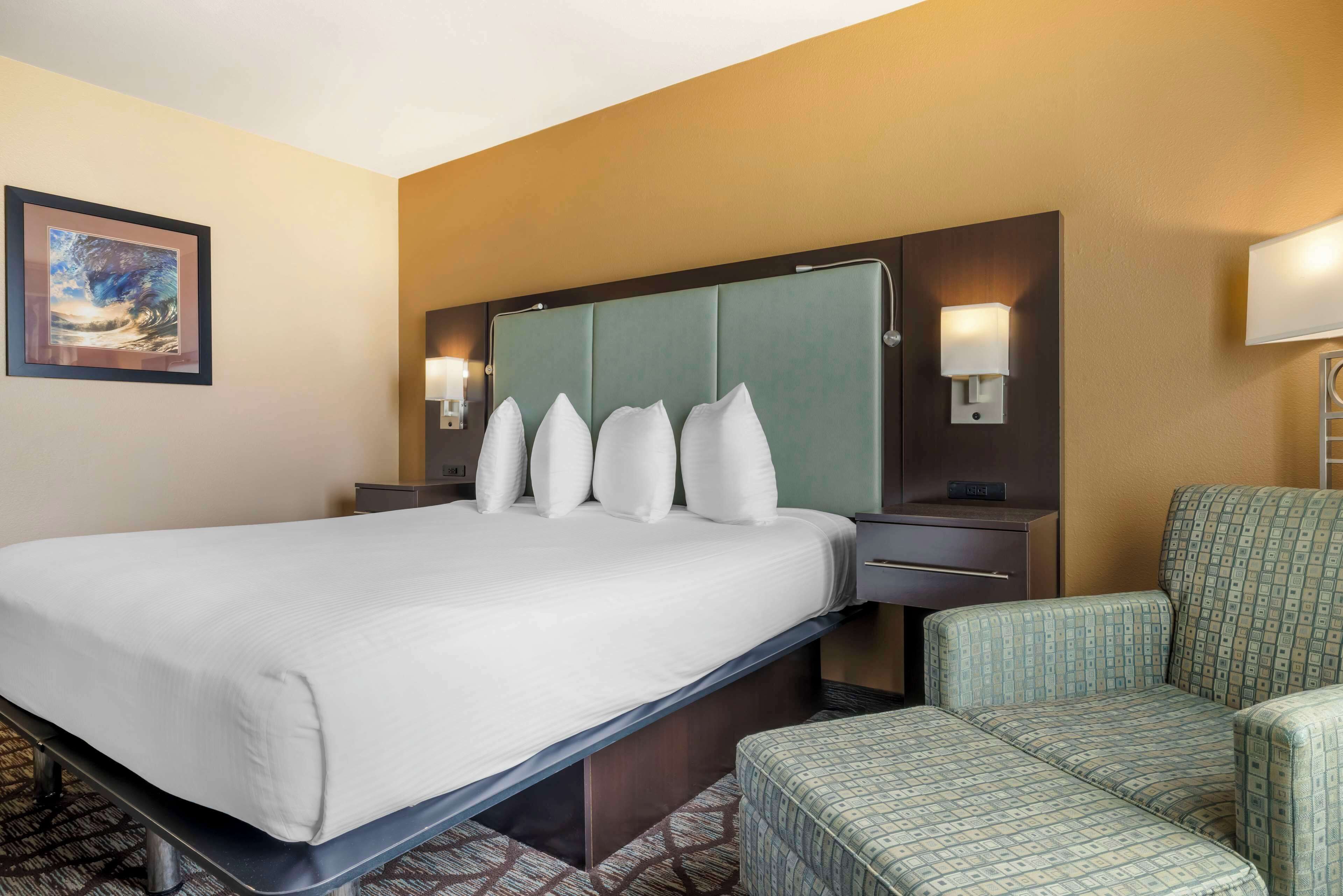 A hotel room with a large bed, two bedside tables, a headboard, and two patterned armchairs.
