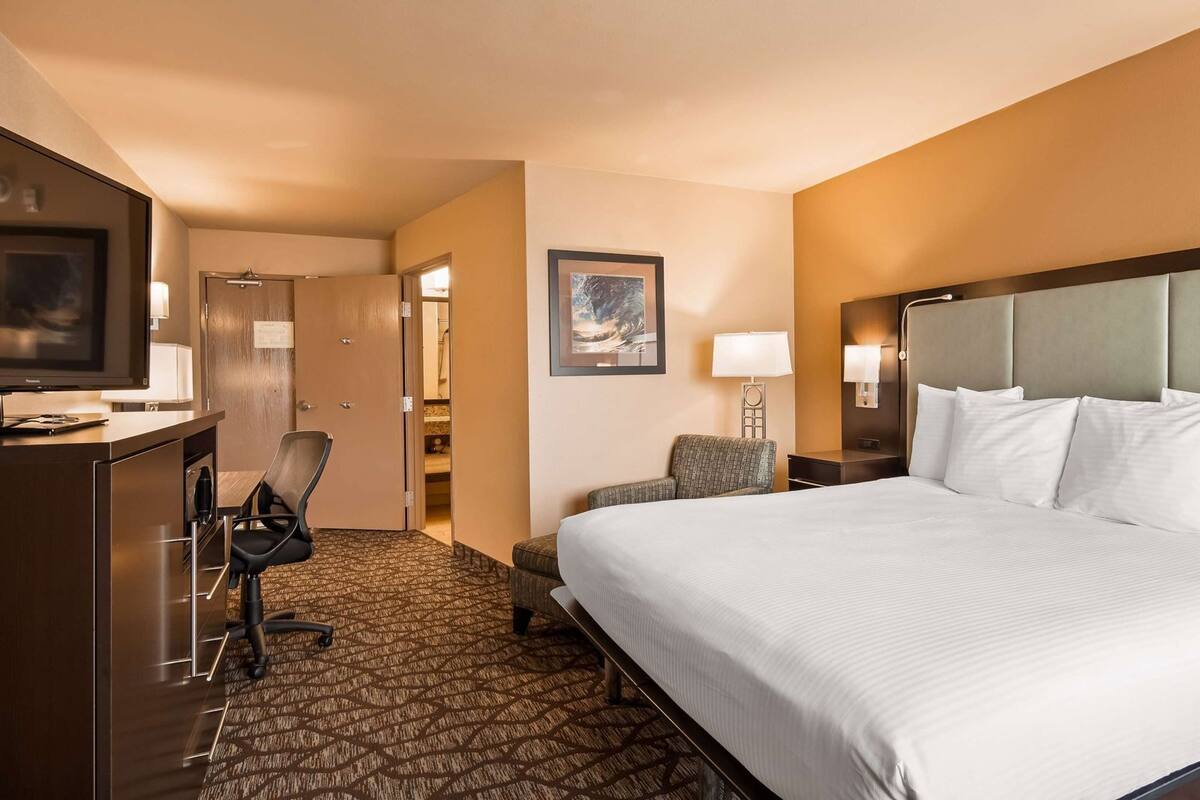 A hotel room with a large bed, a desk, a chair, a nightstand, and a wall-mounted TV.