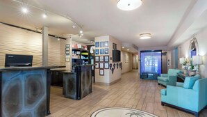 A hotel lobby with a reception desk, a seating area with a sofa, and a television screen. - Best Western Plus Oceanside Palms (Oceanside)