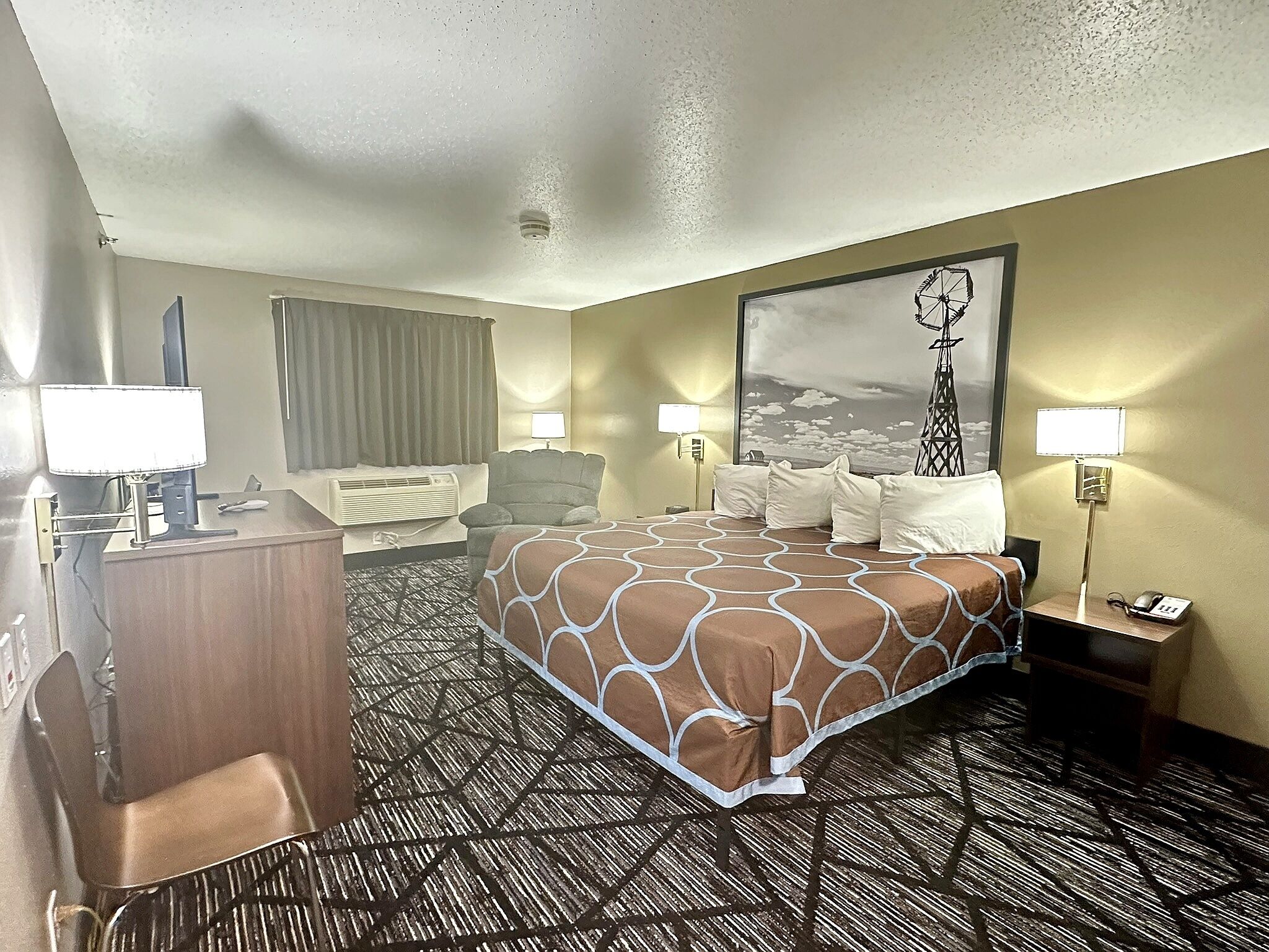 Una habitación de hotel con una cama grande, un escritorio, una silla y una lámpara de escritorio.