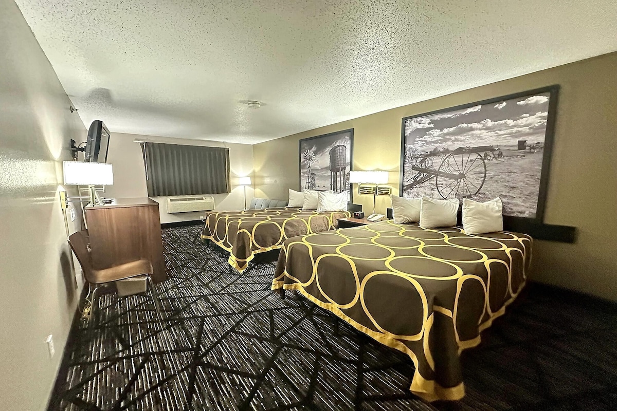 Une chambre d’hôtel avec trois lits, un bureau, une chaise et deux lampes.