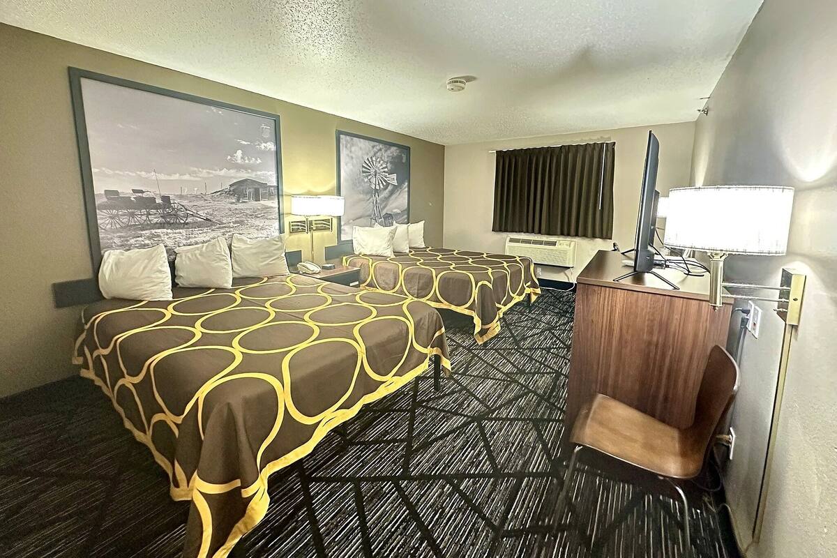 Habitación de hotel con dos camas, un escritorio, una silla, una lámpara de escritorio, un teléfono y un ventanal grande con cortinas.