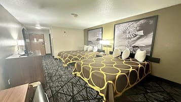 A hotel room with a long bed, a desk, and a chair. There are two wall-mounted lamps and a large window with a windmill painting.