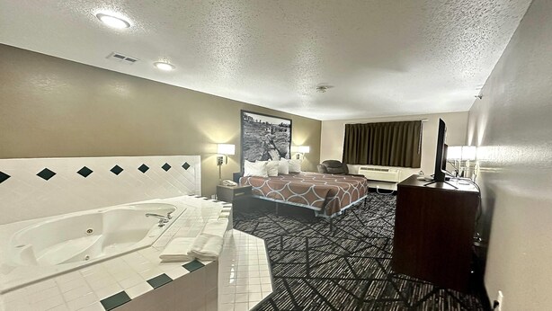 Ein Hotelzimmer mit einer großen Badewanne, einem Bett mit einem gemusterten Überwurf, einem Schreibtisch mit einem Computer und einem an der Wand montierten Fernseher.