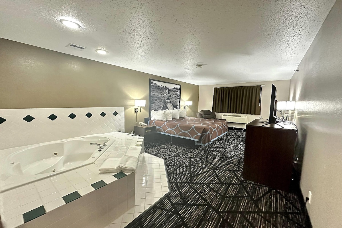 Une chambre d’hôtel dotée d’une grande baignoire, d’un lit avec une couvre-lit à motifs, d’un bureau avec un ordinateur et d’un téléviseur fixé au mur.