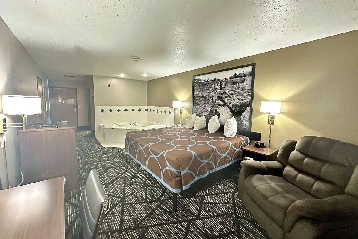 Una habitación de hotel con cama, escritorio, sillón, bañera y una foto grande en la pared.