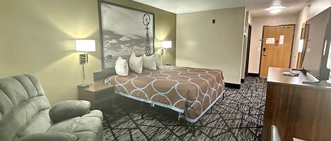Habitación de hotel con una cama grande, una silla, un escritorio con computadora y un cuadro en la pared.
