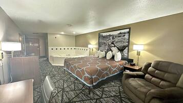 A hotel room with a bed, a sofa, a desk, a lamp, a picture on the wall, and a bathroom with a bathtub and shower.