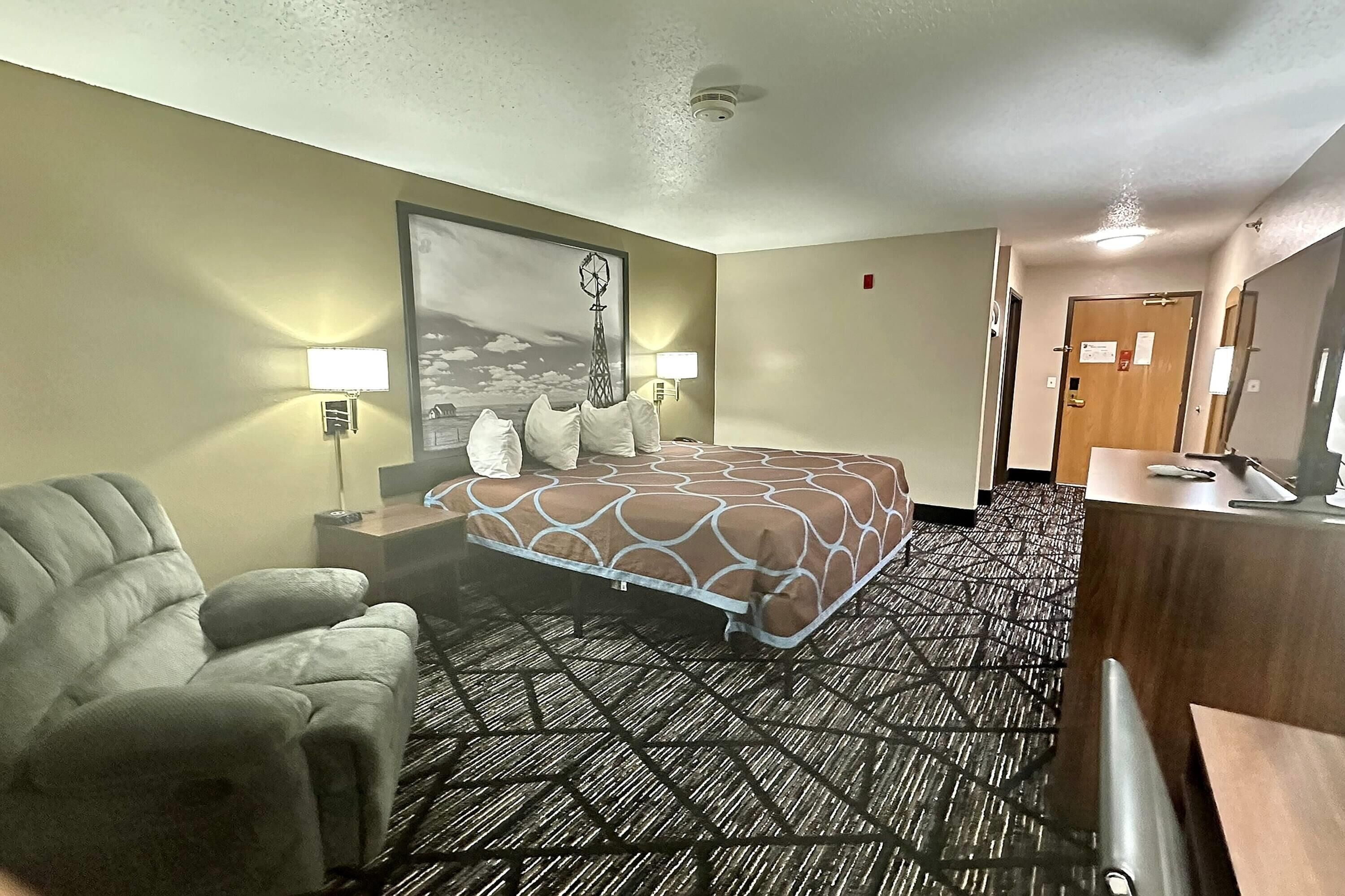 A hotel room with a bed, a chair, a desk, and a lamp.