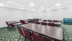 Ein Konferenzraum mit mehreren Tischen und Stühlen, weißen Wänden und einem gemusterten Teppich.