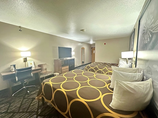 Ein Hotelzimmer mit einem großen Bett, einem Schreibtisch mit Stuhl, einem Fernseher und einem Fenster mit Blick.