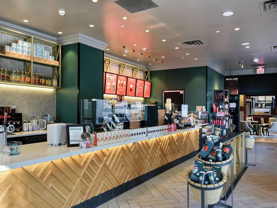 A modern bar area with a wooden counter, shelves with bottles, and a menu board.