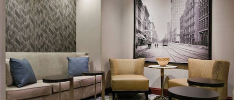 A modern hotel room with a sofa, two armchairs, a small round table, and a large cityscape painting on the wall.