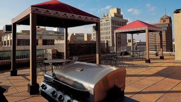Une terrasse extérieure dotée d’un barbecue, d’espaces de repos abrités et offrant une vue sur le panorama urbain.