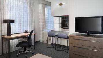 Habitación de hotel con escritorio, silla de oficina, dos taburetes altos, televisor y minibar.
