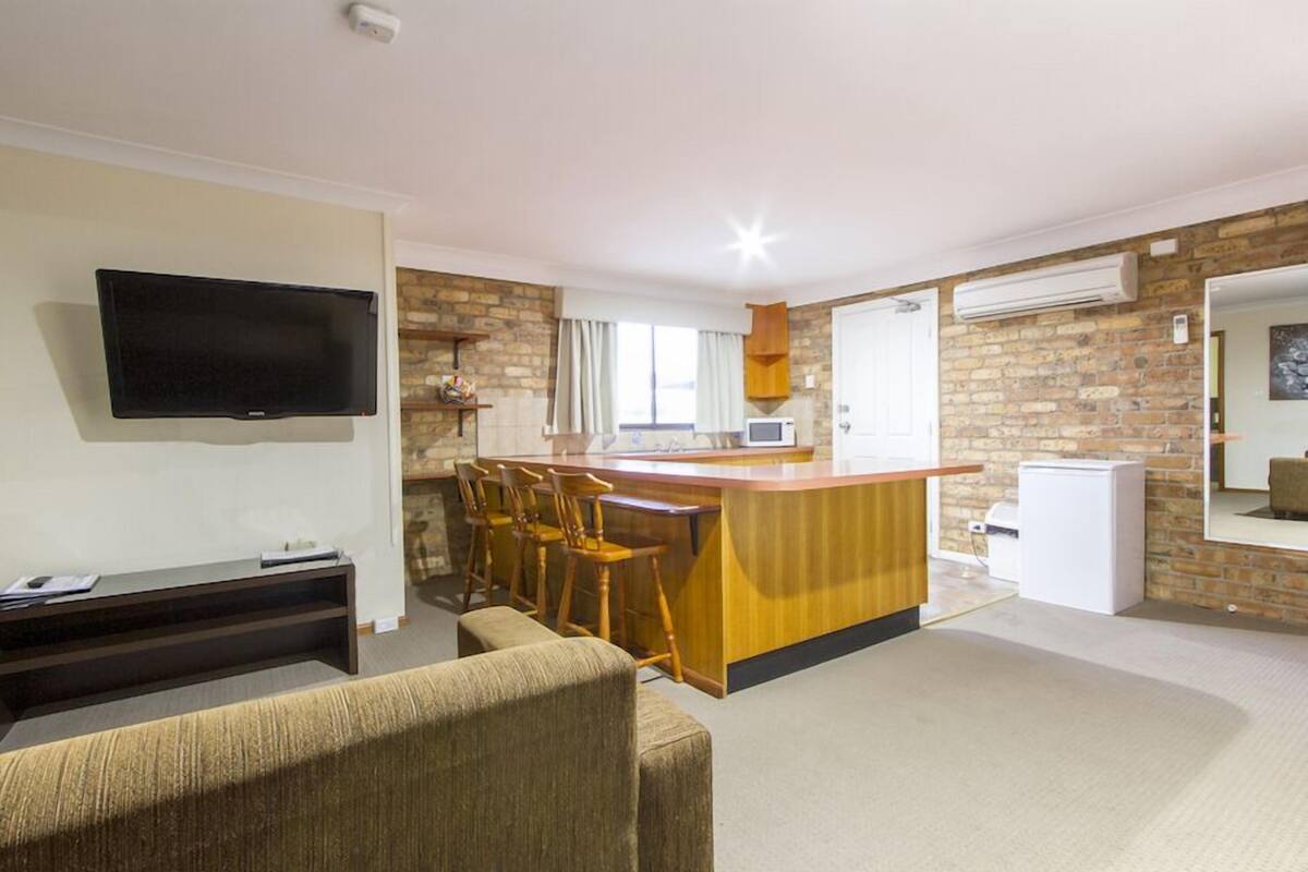 A compact living space with a kitchen area, a flat-screen TV, a sofa, and a bar counter with stools.
