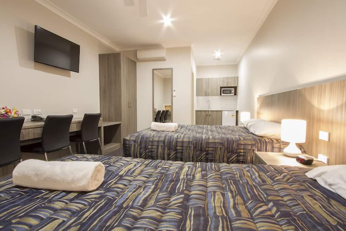 A hotel room with two beds, a desk, chairs, a TV, and a kitchenette.