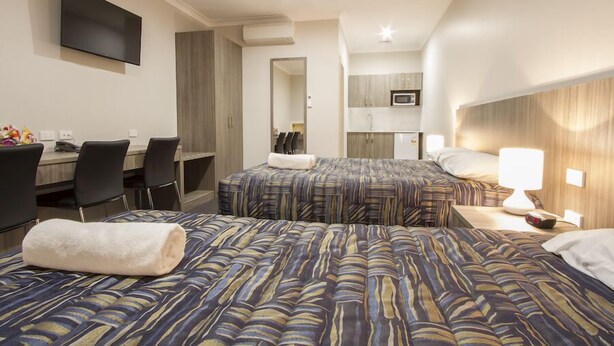 Habitación de hotel con dos camas, un escritorio, sillas, un televisor y una kitchenette.