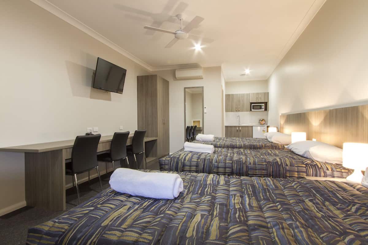 A hotel room with a desk, two beds, a TV, and a kitchenette.