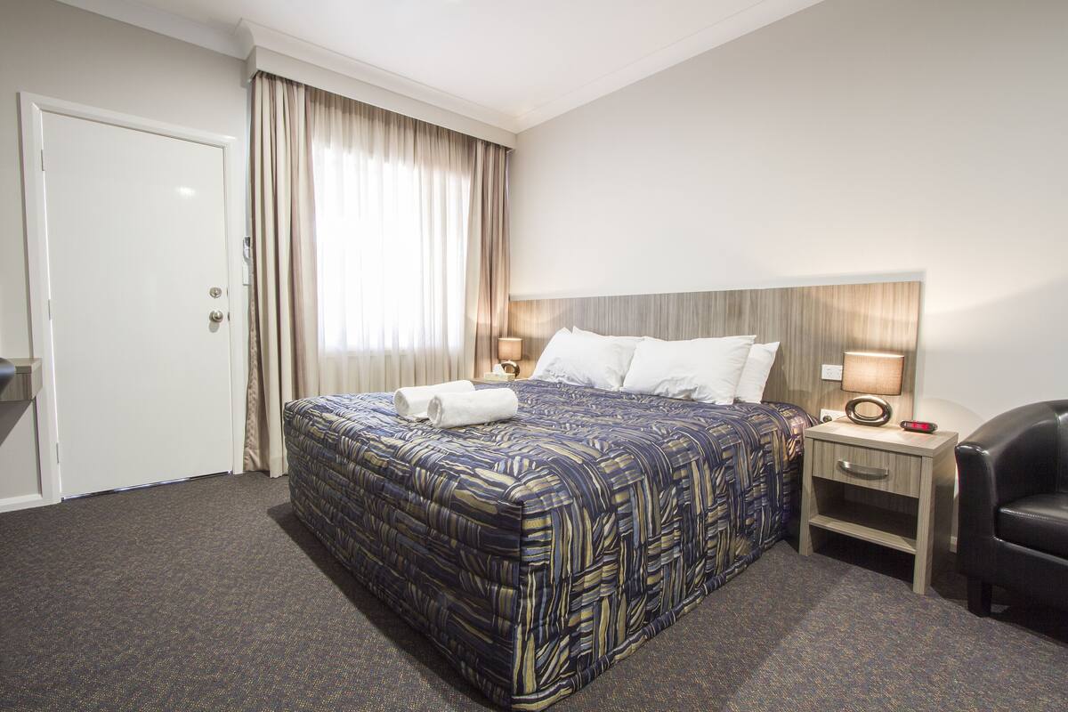 A hotel room with a bed, a nightstand, a chair, a door, and a window with curtains.