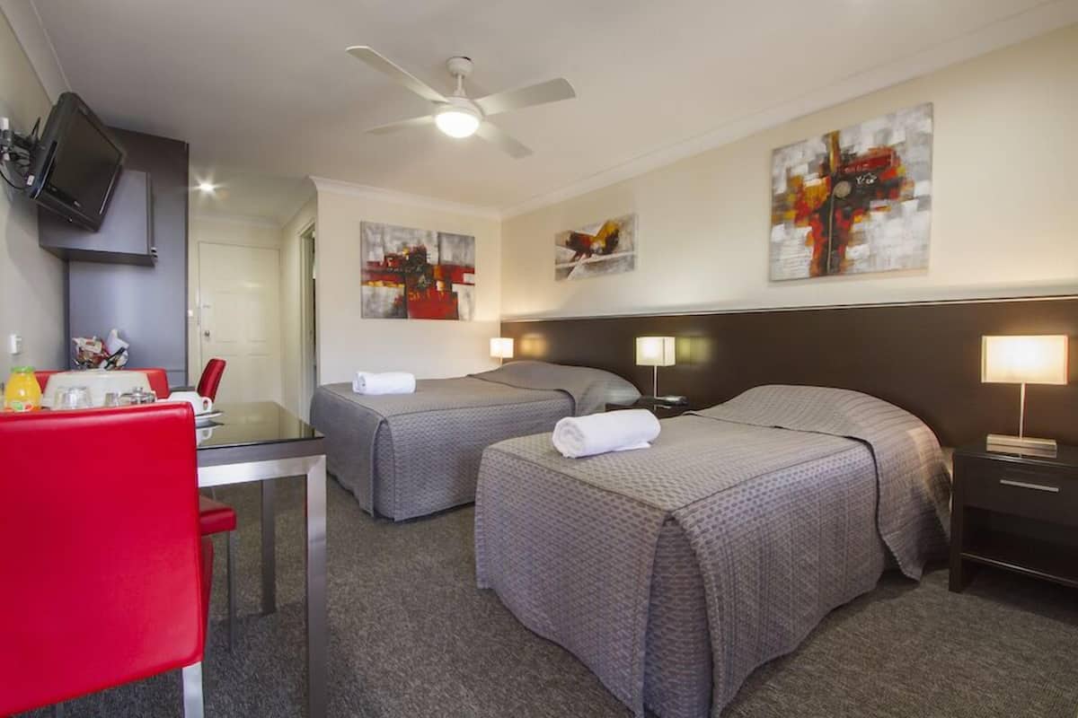 A hotel room with two beds, a desk with a chair, a TV mounted on the wall, and artwork on the walls.