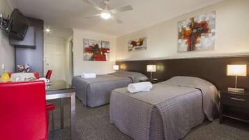 Habitación de hotel con dos camas, un escritorio con silla, televisor montado en la pared y obras de arte en las paredes.