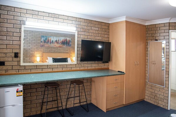 A compact kitchen with a brick backsplash, a flat-screen TV, wooden cabinets, and a bar stool.