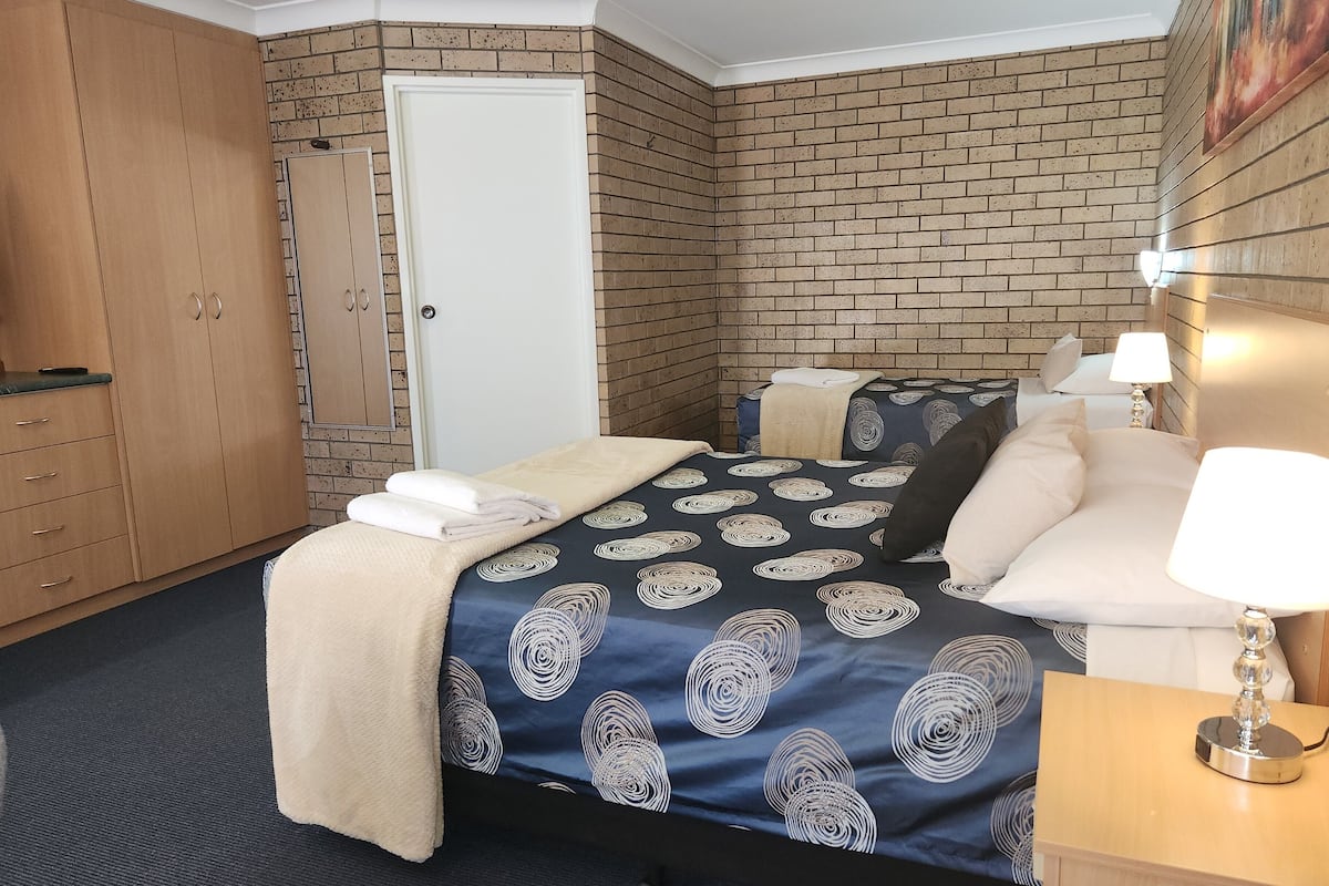 A hotel room with two beds, a wardrobe, a door, and a painting on the wall.