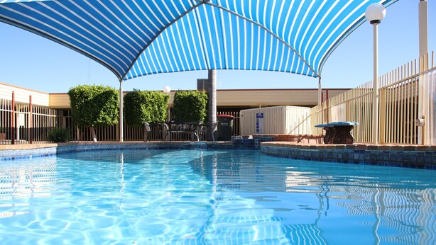 A swimming pool with a blue and white striped canopy, surrounded by a fence and potted plants. - Macintyre Motor Inn (Goondiwindi)