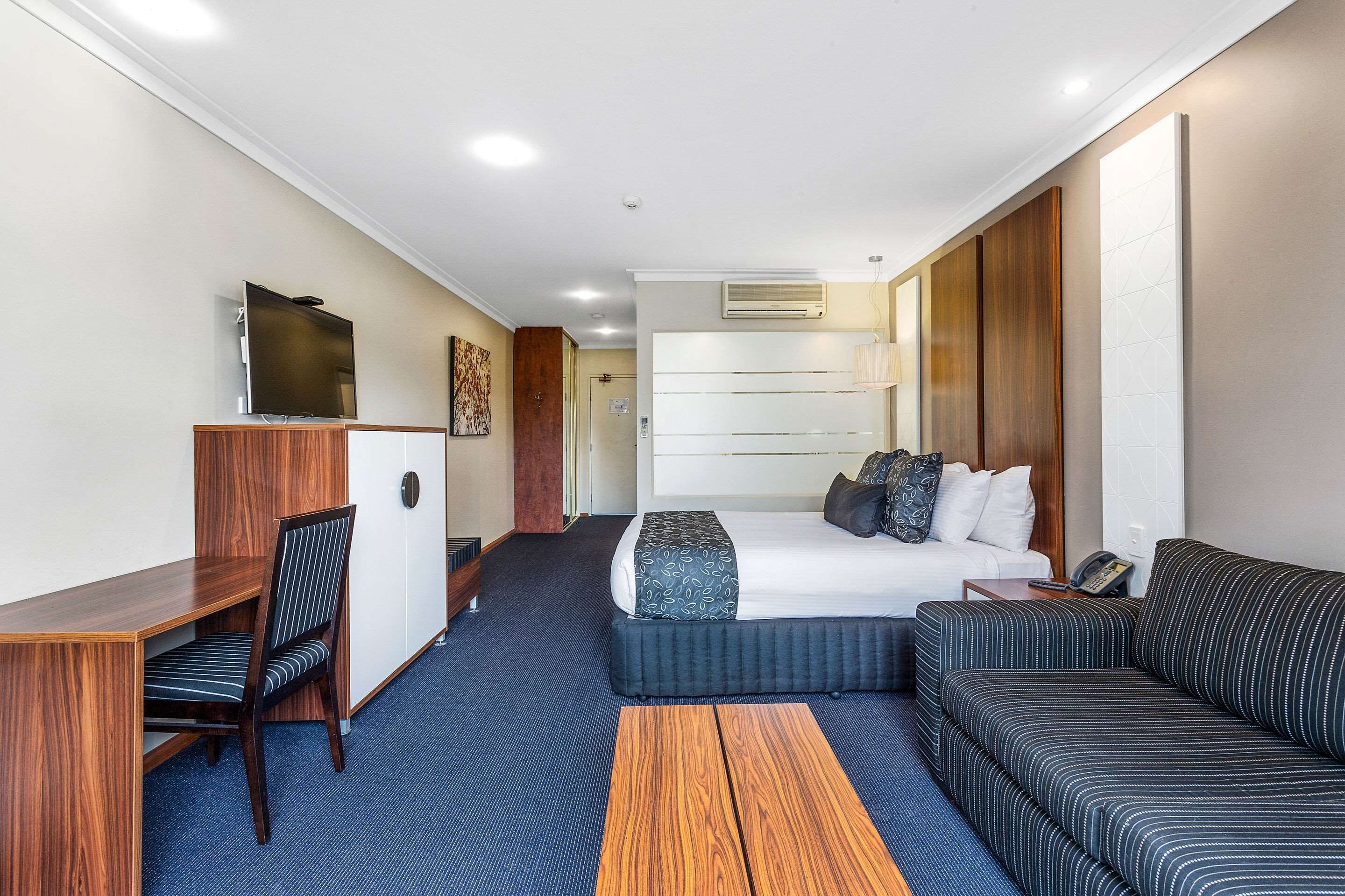 A hotel room with a bed, a desk, a chair, a sofa, and a small table.