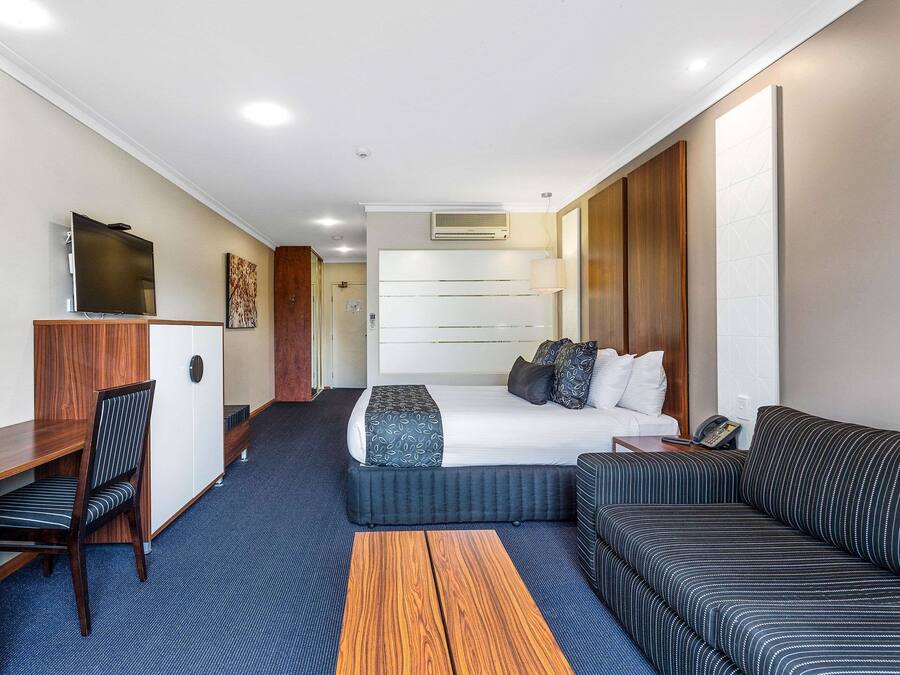 A hotel room with a bed, a desk, a chair, a sofa, and a small table.