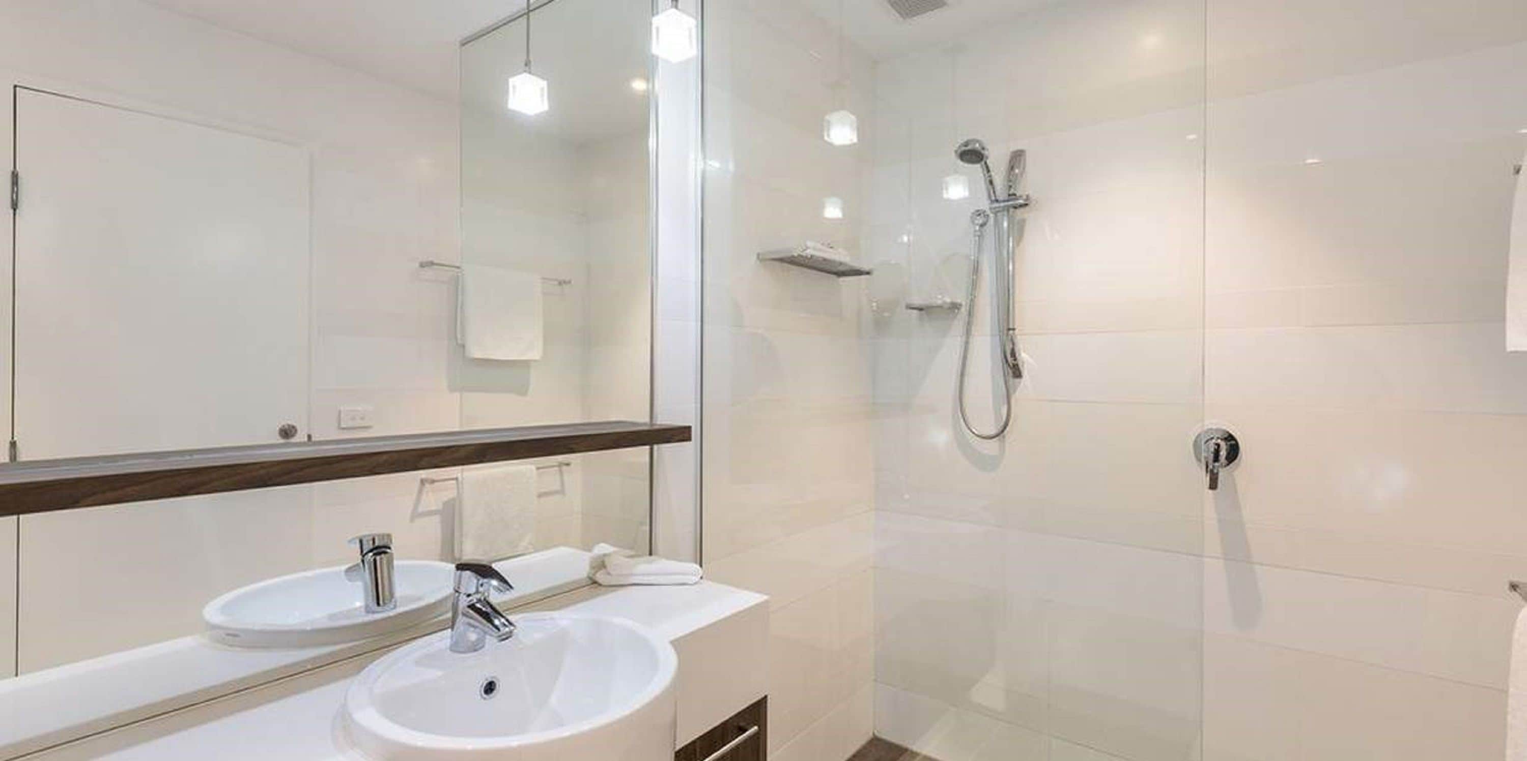 Un baño moderno con ducha envuelta en vidrio, tocador doble y un espejo grande.