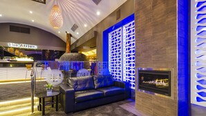Una moderna hall con un divano in pelle nera, un tavolino con una pianta, un caminetto e una parete decorativa illuminata di blu.