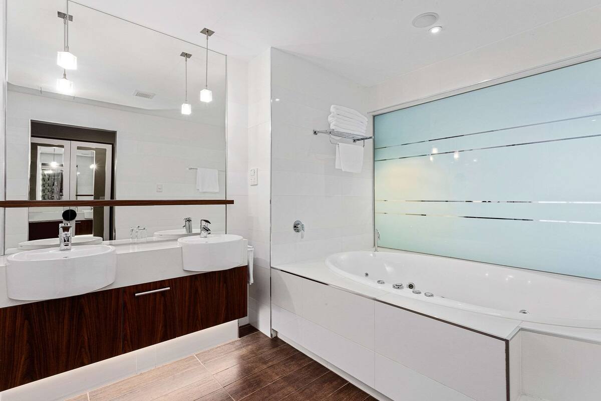 Un baño moderno con dos lavamanos, un espejo grande y una bañera independiente.