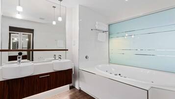 A modern bathroom with two sinks, a large mirror, and a freestanding bathtub.