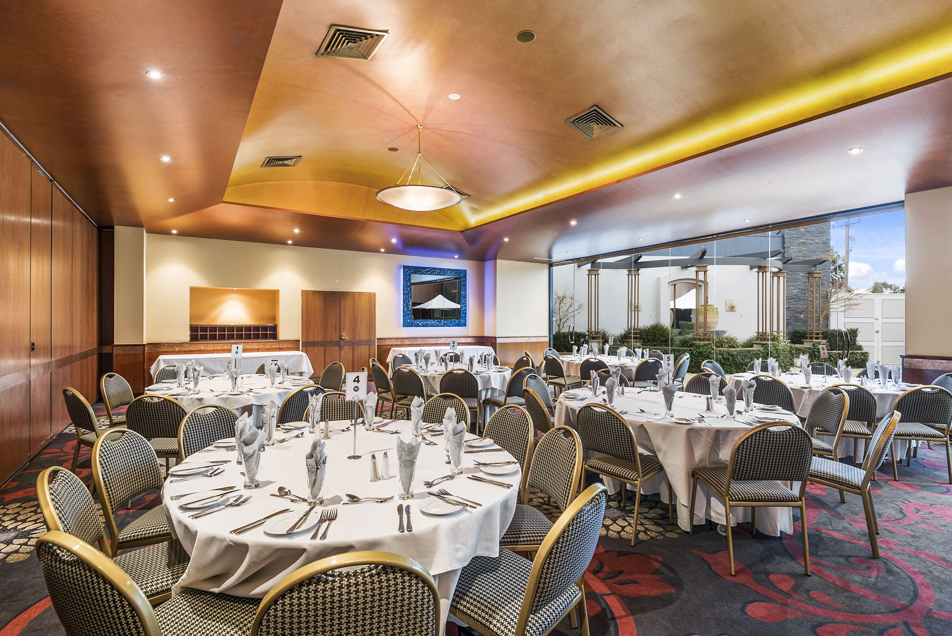 A banquet hall with round tables, chairs, and a large window offering a view.