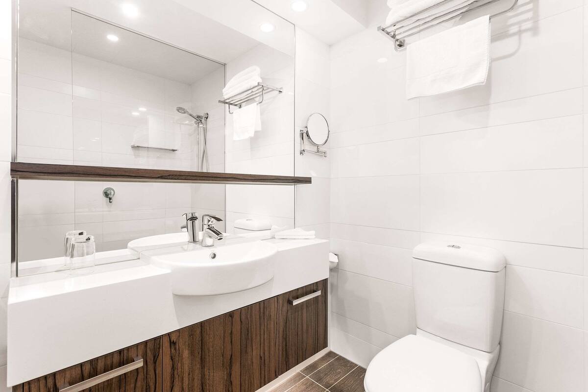 Un baño moderno con un espejo grande, dos lavamanos, un inodoro y una ducha.